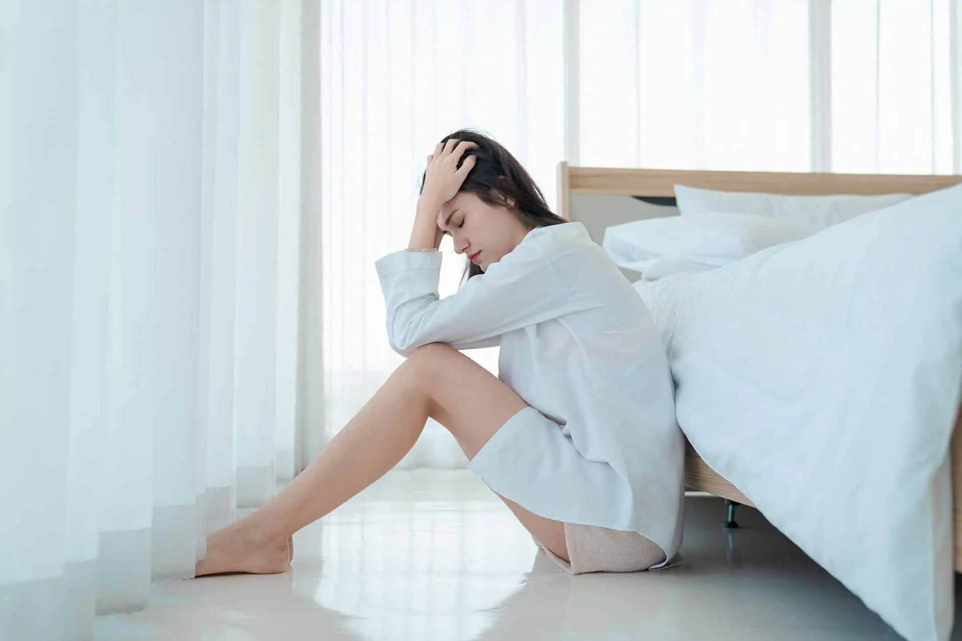Asian young woman sitting sad beside the bed in bedroom