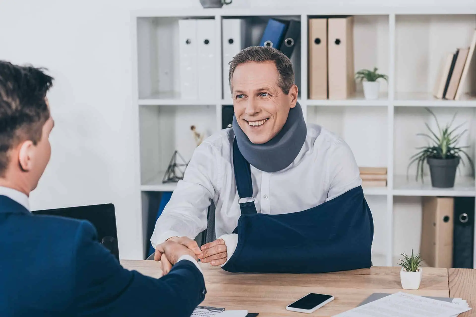 Worker in neck brace with brokenarm and businessman in blue jacket shaking hands