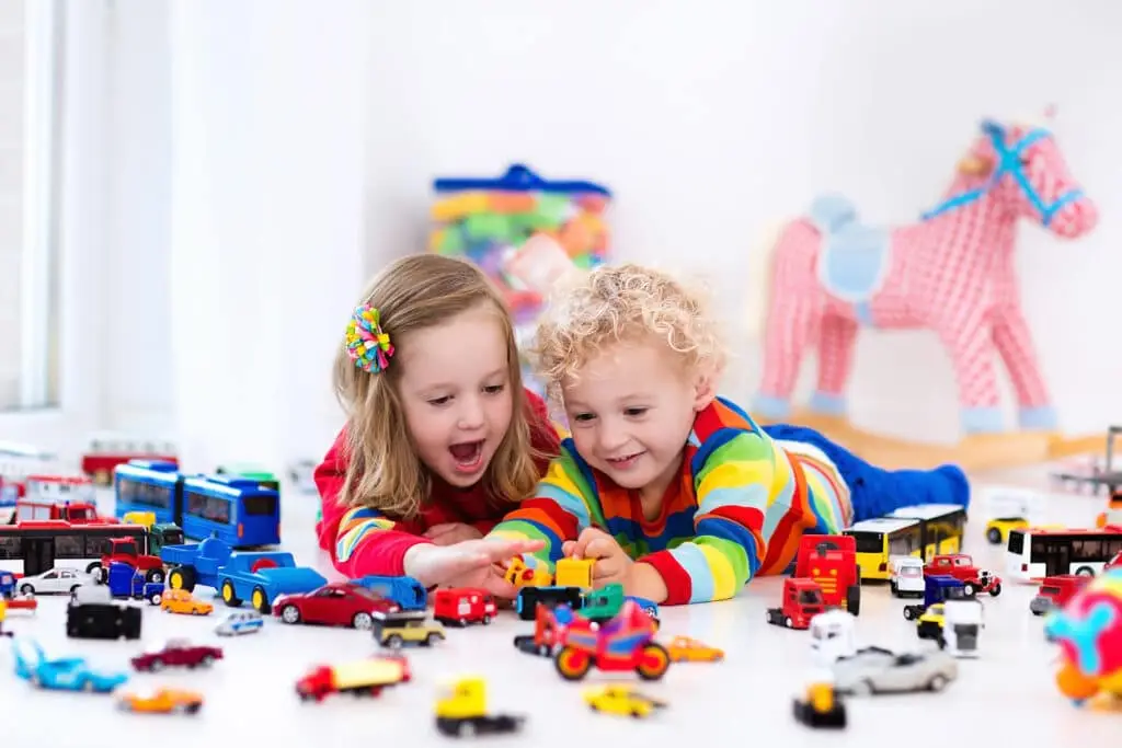 Little toddler boy and girl playing with model car collection on the floor.