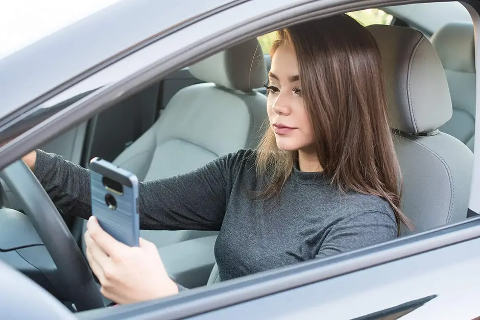 Happy teen girl driving a new car while texting