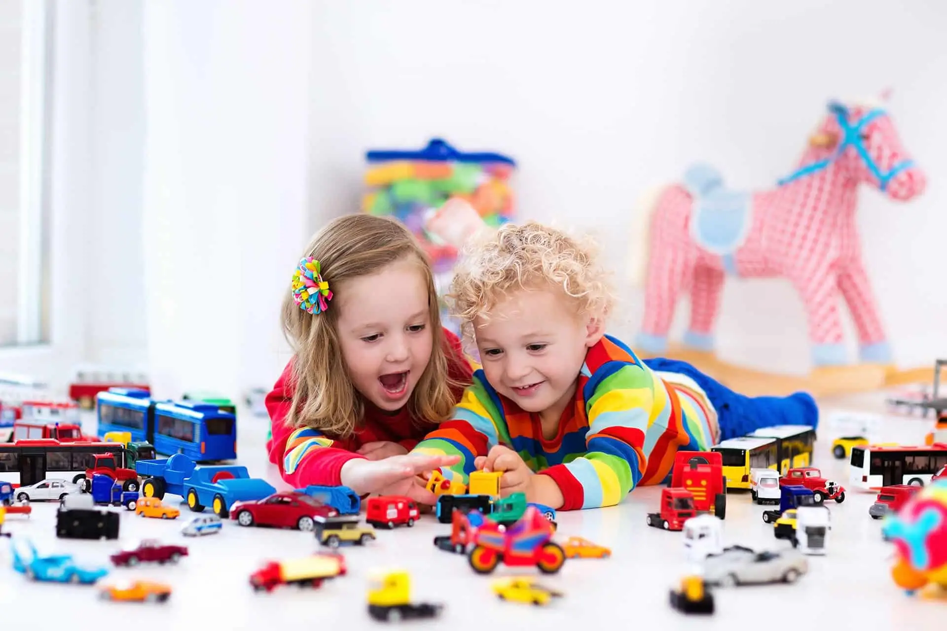 Little toddler boy and girl playing with model car collection on the floor.