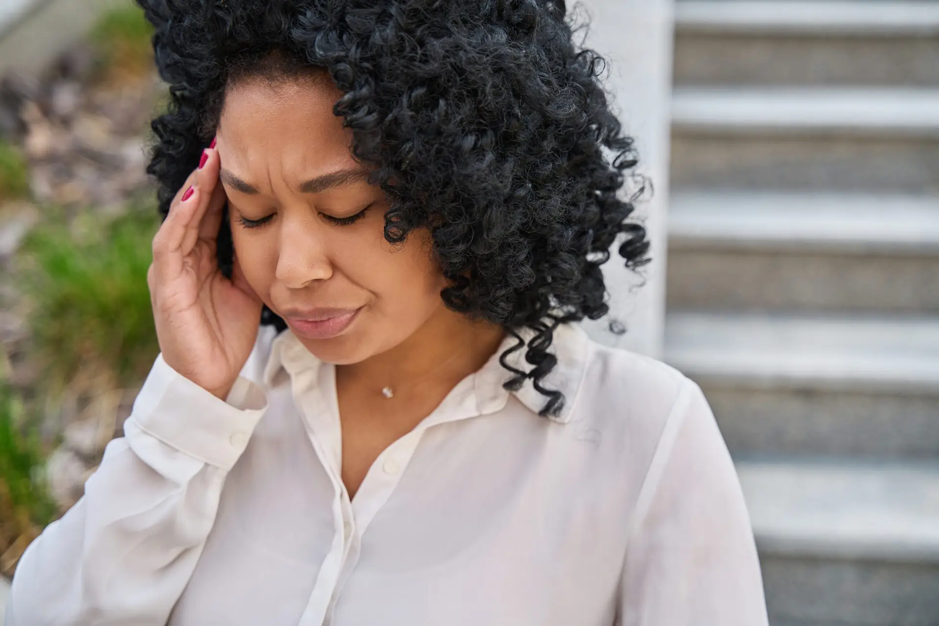 woman wearing a white blouse rubbing her temple from a persistent headache after an accident