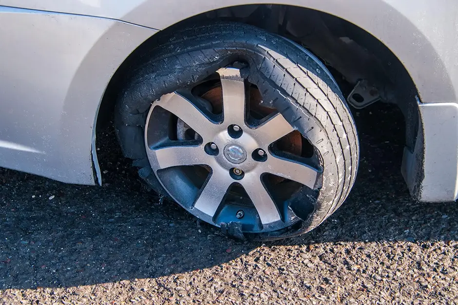 Car tire that has a blowout with rim and car damage.